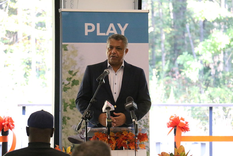 man speaking at multiple microphones with banner with the word