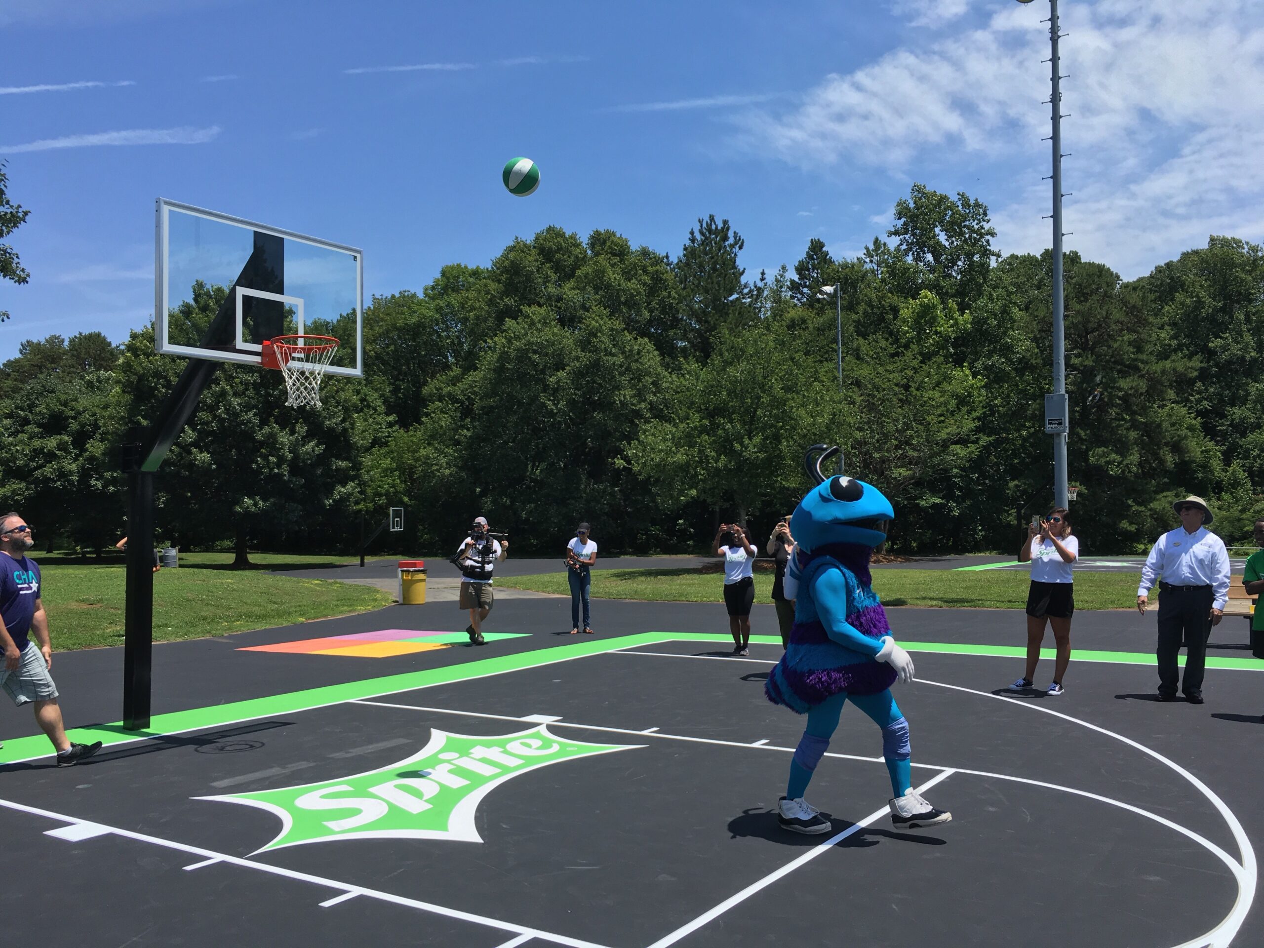 Adults playing basketball outside including a person dressed in a blue hornet costume
