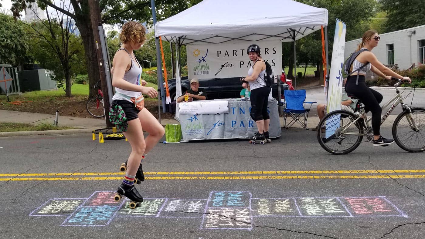 Adult playing hopscotch near a Partners for Parks booth
