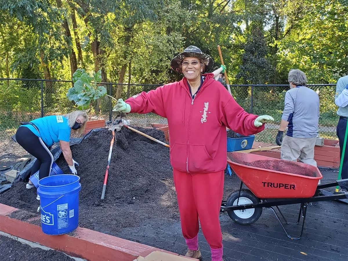 Woman in red sweats posing in front of people working on a dirt pile