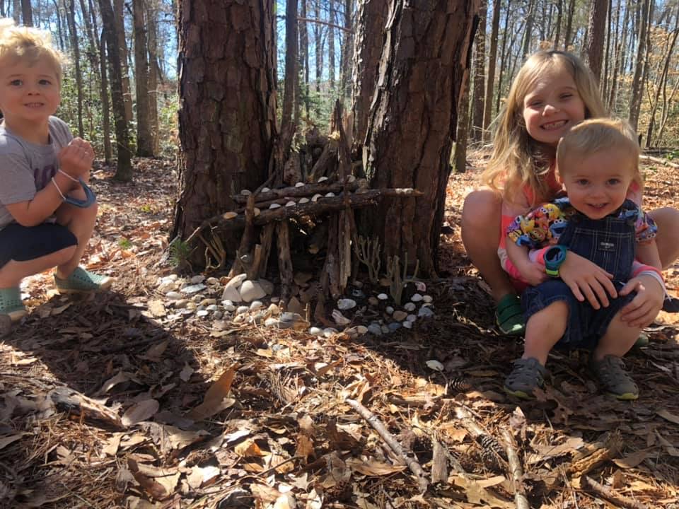three young children sitting in the forest near a tree