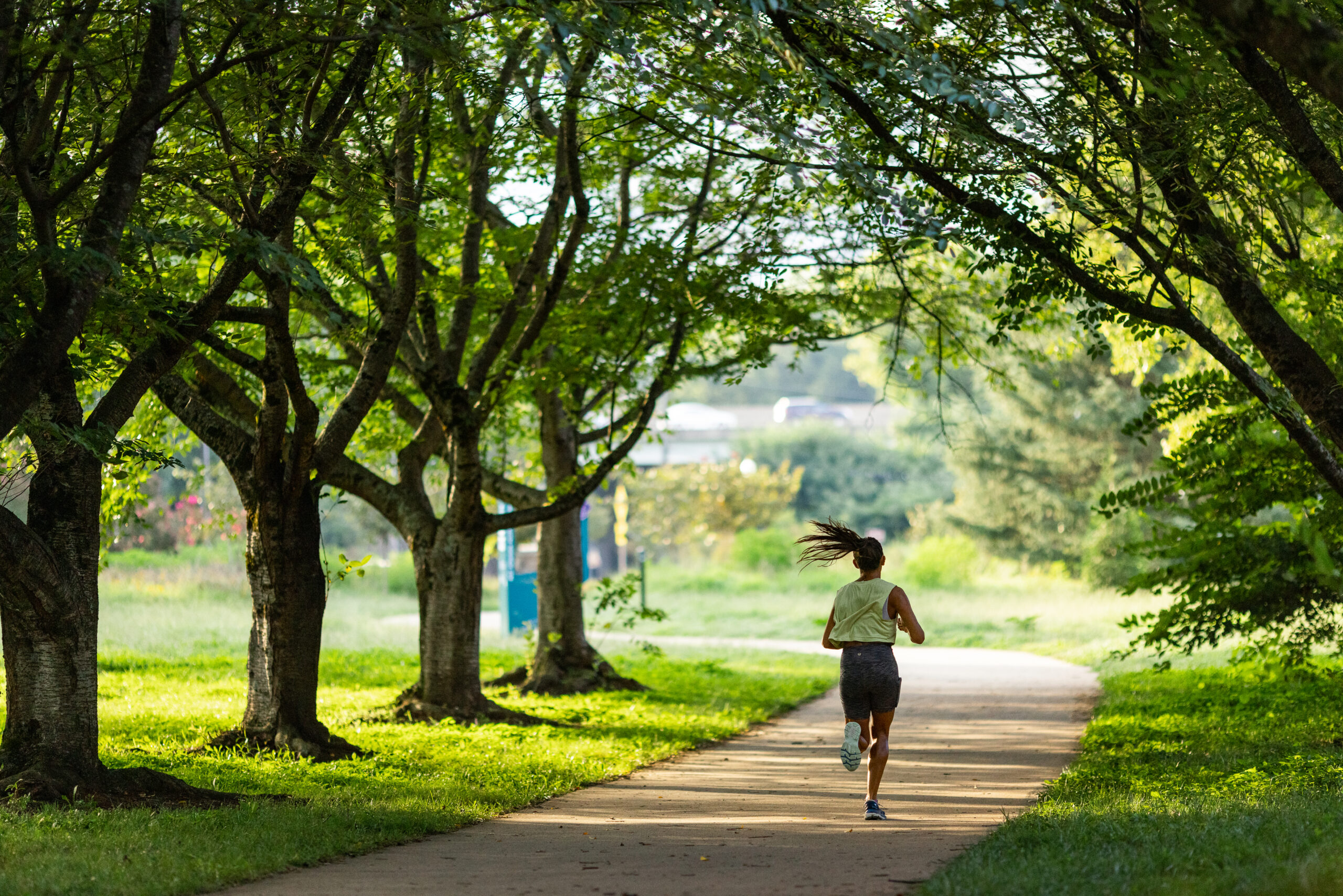 woman jogging through a park path with trees