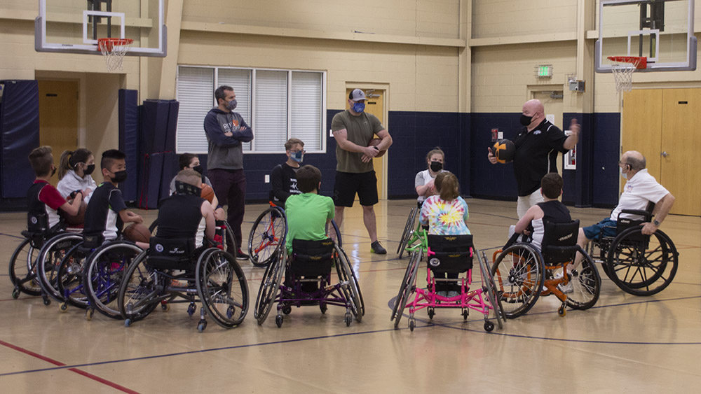 group of children in wheelchairs circled around 4 coaches in a gymnasium