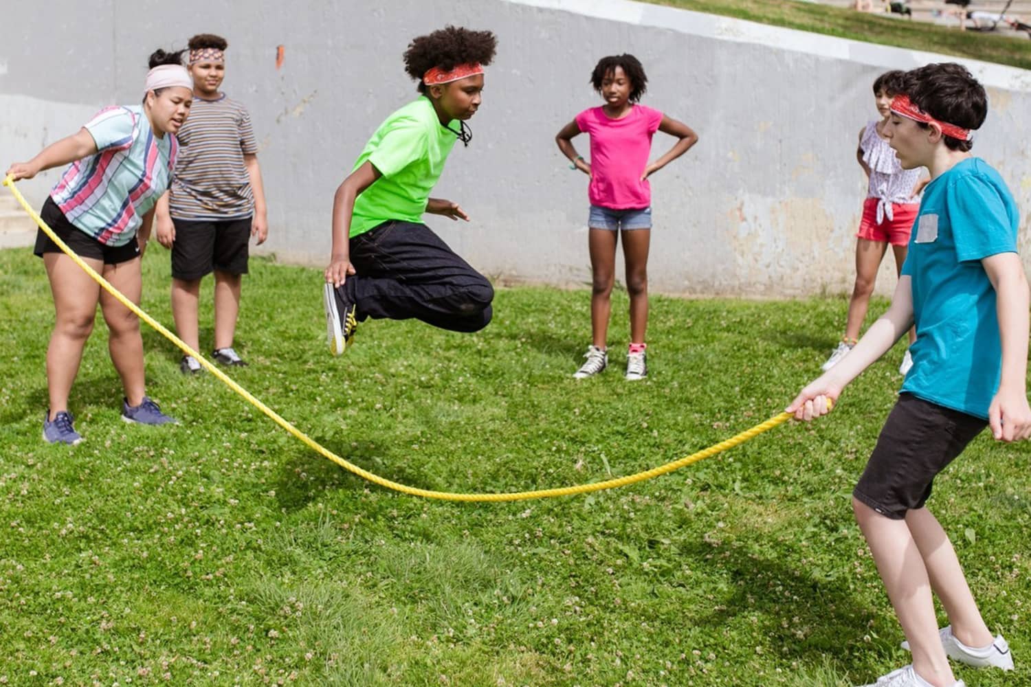 group of six children playing jump rope in the grass